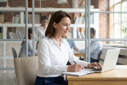 Femme d'environ 50 ans au bureau moderne en blouse blanche